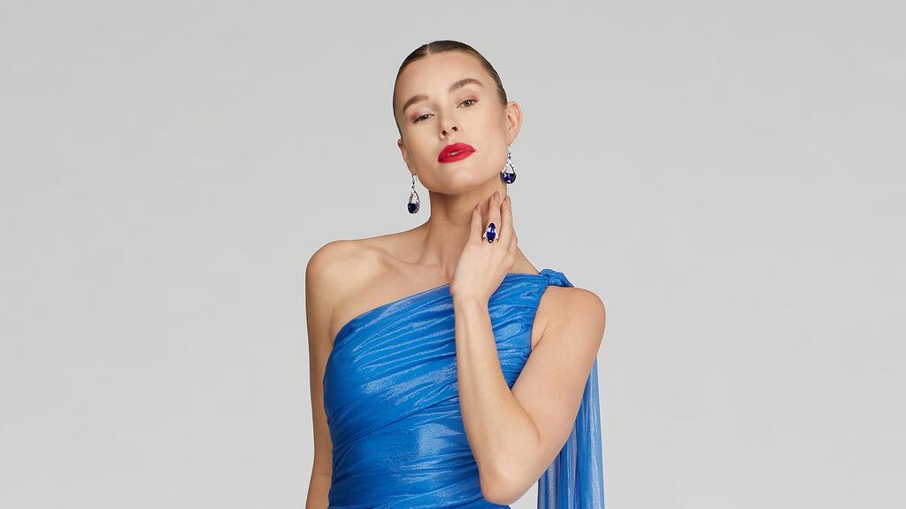 Martin Katz’s half-moon tanzanite earrings paired with a blue one-shoulder Halston gown and a ring from the jewelry brand featuring a 14.5-carat oval tanzanite with trapezoid diamond sides Blue Halston gown and Martin Katz tanzanite earrings and ring