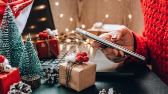 The first predictions about the 2024 holiday season have begun rolling in, with Deloitte forecasting 2 to 3 percent retail sales growth and a “solid” holiday overall, and Adobe Analytics touting the importance of mobile shopping and generative AI. Stock image of hand holding phone by keyboard