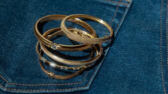 A selection of gold bracelets and bangles from Signet Jewelers-owned banner Zales. Signet posted Q1 sales of $1.54 billion, up 2 percent year-over-year. Gold and diamond bangles on a pair of jeans